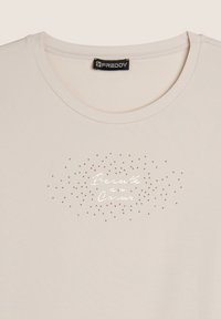 T-shirt di cotone beige chiaro con scollatura rotonda; presenta una stampa decorativa con la scritta "Beauté au Cœur" in argento e piccoli punti dorati.