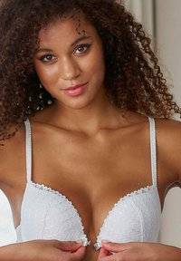 White lace-trimmed plunge bra with embossed zigzag texture, adjustable straps, and hook closure, featuring a seamless design for comfort.