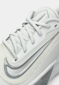 Vit sneakers med texturerat tyg, framträdande grå Nike-swoosh och snörning fram. Har en slät, formad sula och präglade detaljer.