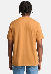 Kortærmet t-shirt i sennepsgul, med et enkelt design, lige snit og en glat tekstur som bomuld. Sømdetaljer ved kraven.