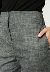 Graue karierte Hose mit glattem Stoff, seitlichen Taschen und flachem Bund. Der Stoff zeigt ein dezentes eingewebtes Muster.
