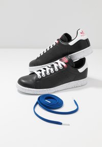 Svarta lädersneakers med vita sulor som har blå prickar. Snörda med vita skosnören, tillsammans med extra blå snören.