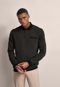 Dunkelgrünes Langarm-Polohemd mit navyfarbenem Kragen, Knopfleiste und Brusttasche. Glatte Textur mit gerippten Bündchen und Saum.