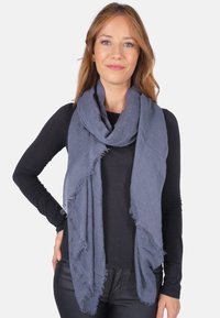 Écharpe texturée bleu foncé avec des bords effilés, drapée autour du cou, superposée à un haut noir à manches longues.