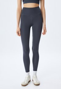 Højtaljede, marineblå leggings lavet af glat, strækbart stof. Har et elegant design og sømløs konstruktion, parret med hvide atletiske sneakers.