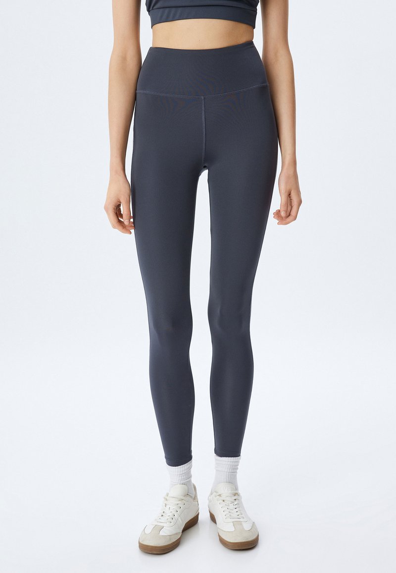 Hoge taille, marineblauwe leggings gemaakt van gladde, rekbare stof. Kenmerkt een slank ontwerp en naadloze constructie, gecombineerd met witte sport sneakers.