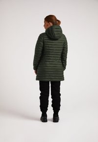 Zelený prošívaný kabát s kapucí, s vodorovným prošíváním, dlouhými rukávy a slim fit. Nese se s černými tepláky a botami.