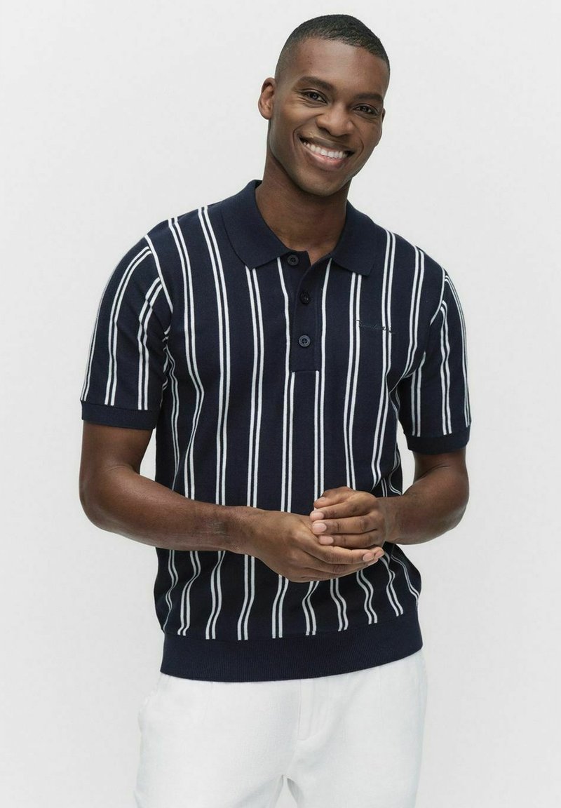 Mörkblå stickad polo med vita vertikala ränder, med krage och treknappsknäppning; figurnära design med ribbstickad nederkant och muddar.