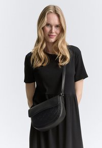 Borsa a tracolla nera in pelle con design curvo, caratterizzata da testo in rilievo e una lunga tracolla. Texture liscia e stile minimalista.