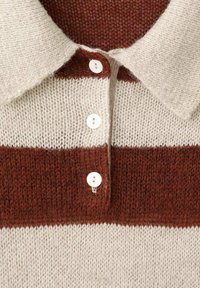 Polo de punto con rayas crema y óxido, con cuello y tres botones blancos. Textura suave con una trama holgada.