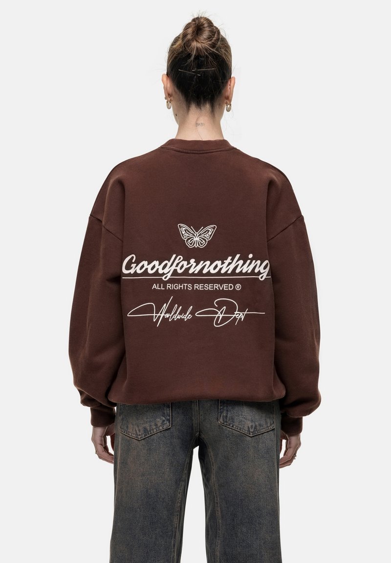 Felpa oversized marrone con una grafica di una farfalla e il testo "Goodfornothing" sulla schiena; presenta spalle scese e polsini a coste.