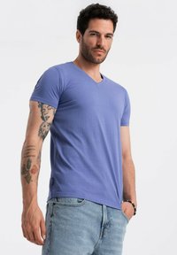 T-shirt a maniche corte con scollo a V in cotone viola chiaro, caratterizzato da un design aderente e un orlo dritto. Indossato con jeans in denim azzurro chiaro.