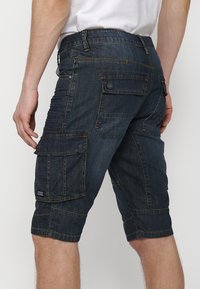 Shorts cargo in denim blu scuro, con multiple tasche laterali, dettagli cuciti e una vestibilità comoda con taglio fino al ginocchio.