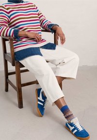 Striped knit sweater in cream, red, blue, and brown; denim underlay; white cropped pants; blue sneakers with white stripes; patterned socks.