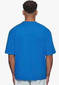 Blå kortærmet t-shirt lavet af bomuld. Har en afslappet pasform, rund halsudskæring og en blød, glat tekstur. Synlige sømdetaljer ved sømmene.