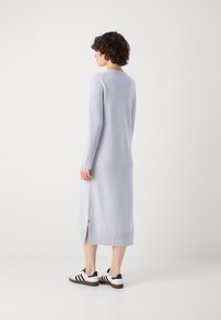 Lyseblå lang genserkjole med ribbede sidepaneler, sidesplit, og strukturert kant, parret med hvite sneakers med svarte detaljer.