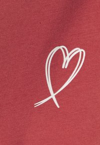 Roter Baumwollstoff mit feiner Textur zeigt ein weißes Herzdesign. Das Herz hat sanfte Kurven und ein fließendes Aussehen.