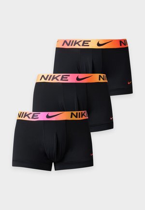 Modèle masculin debout, pieds nus, portant un boxer Nike noir avec une ceinture orange et rose, sur fond blanc uni.