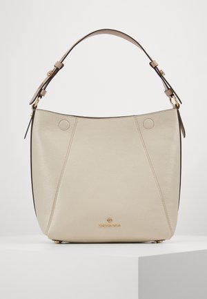 Sac à main en cuir beige de Michael Kors avec une seule bandoulière, des détails de couture subtils et un logo doré sur le devant, posé sur une surface blanche.