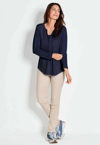 Dunkelblaues Langarmoberteil mit rundem Halsausschnitt, kombiniert mit beigen Slim-Fit-Hosen. Die Sneakers haben ein blau-graues Design mit strukturierten Sohlen.