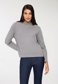 Szary sweter z okrągłym dekoltem, długimi rękawami i luźnym krojem, zestawiony z ciemnoniebieskimi dżinsami. Materiał wydaje się miękki i gładki.