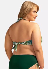 Zestaw bikini z białym topem w zielony print liści i zawiązaniem, w połączeniu z jednolitymi ciemnozielonymi majtkami. Materiał wydaje się gładki i miękki.