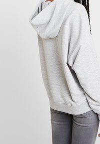 Grå hoodie av mjukt tyg med huva, sänkta axlar och ribbade muddar, kombinerad med smala grå jeans.