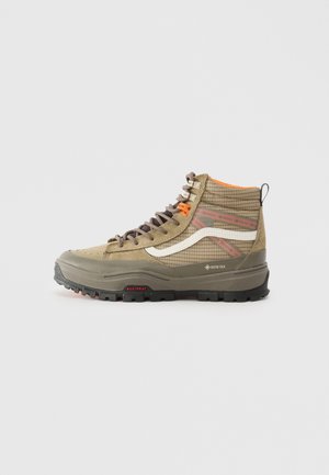 Botte de randonnée montante beige avec semelle en caoutchouc épaisse, bande blanche latérale, étiquette Gore-Tex, lacets marron et doublure intérieure orange sur fond uni.
