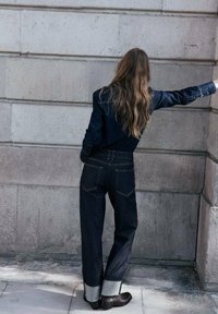 Jeans in denim scuro con vestibilità rilassata, orlo risvoltato, tasche posteriori e cuciture a contrasto. Abbinati a una giacca in denim dello stesso colore.