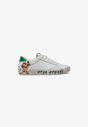 Scarpa da ginnastica bianca con linguetta verde sul tallone, personaggio dei cartoni animati che mostra il muscolo vicino al tallone, e testo "STAY STRONG" su una suola dall'aspetto sporco.