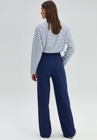 Striped long-sleeve shirt in white and navy, paired with loose navy pants featuring an elastic waistband. Smooth fabric, relaxed fit.
