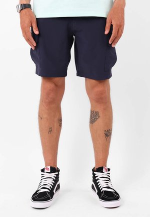 Shorts bleu marine en tissu léger, dotés de deux poches latérales et d'un ourlet propre. Associés à des baskets montantes noires.