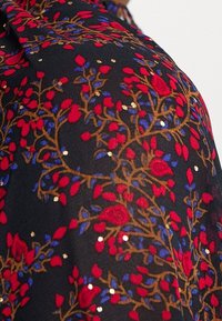 Tessuto nero con un motivo floreale caratterizzato da petali rossi e blu, accenti dorati e intricati viticci marroni; texture trasparente con paillettes.