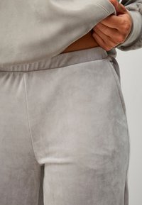 Ensemble de détente en polaire gris clair mettant en avant une texture douce, une ceinture élastique et un design épuré. Gros plan sur les matériaux et les détails de couture.
