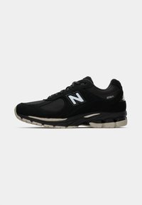 Black athletic shoe with mesh and suede materials; features a thick sole, neutral accents, reflective logo, and padded collar.
