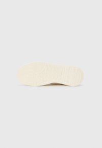 Shoe sole in off-white rubber with a textured grip pattern. Features raised lines and an embossed logo near the heel for stability.