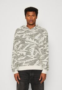 Hoodie u svijetlosivoj boji, s teksturiranim chevron uzorkom u tamnijoj sivoj. Riblje manžete i rub, s vezicom na kapuljači.