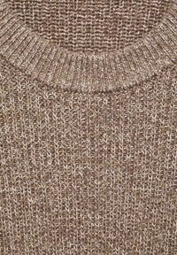 Close-up van een gemêleerde beige en bruine gebreide trui met een gedetailleerde geribbelde ronde halslijn en een gestructureerd verticaal breipatroon.