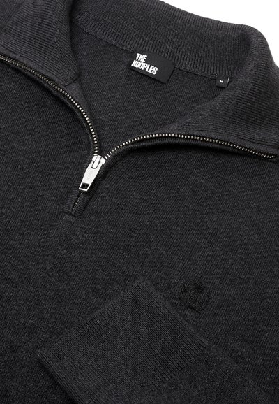 Zwarte gebreide zip-up trui van zacht materiaal. Heeft een geribbelde kraag en manchetten, een zilveren rits en een subtiele logo-detail op de borst.