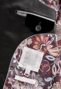Tessuto nero con un motivo paisley in tonalità di rosso, viola e marrone. Presenta una tasca in velluto nero con un bottone e un'etichetta bianca.
