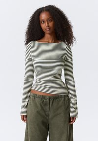 Zeleno-bela majica z dolgimi rokavi v črte, z odprtim izrezom okoli vratu in oprijetim krojem. Kombinirana z ohlapnimi olivno zelenimi hlačami.
