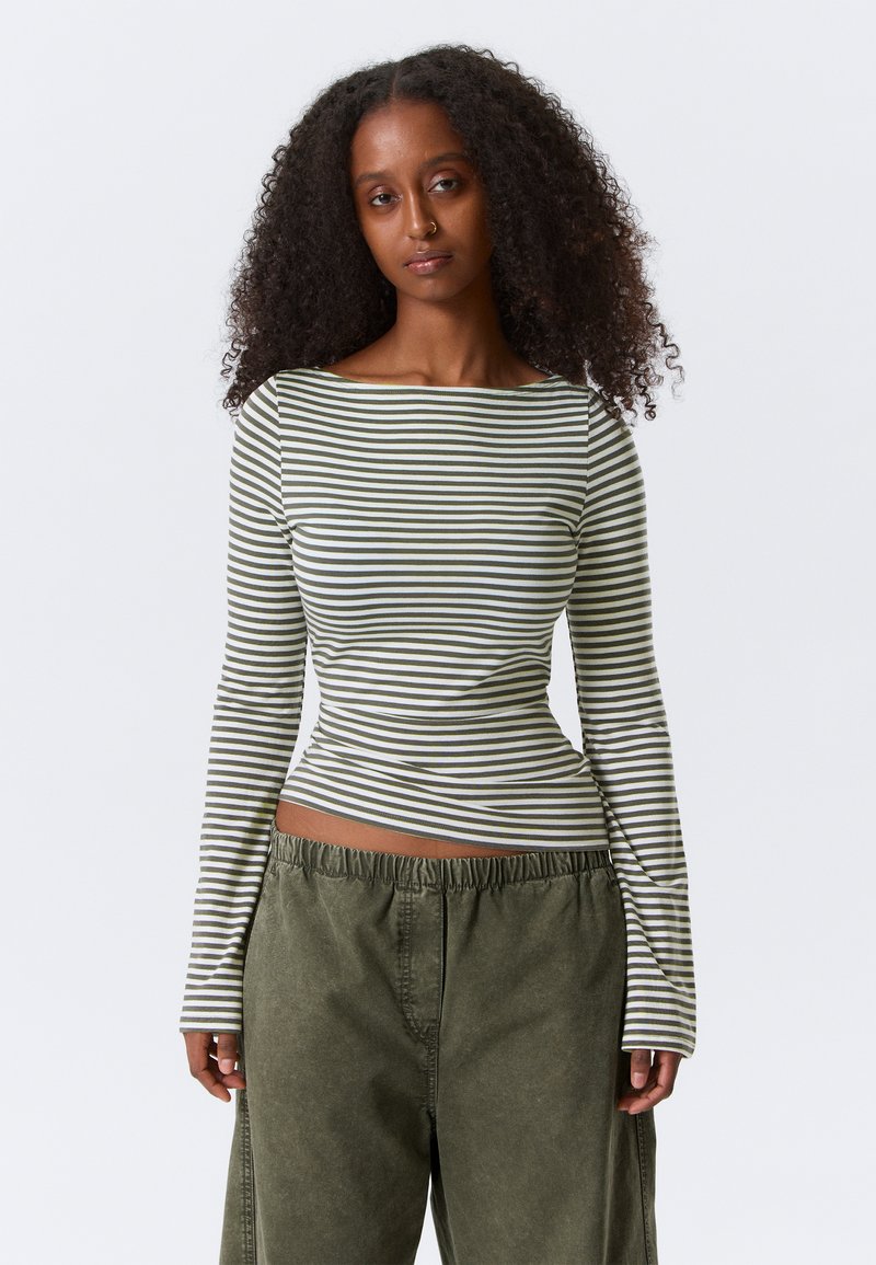 Zeleno-bela majica z dolgimi rokavi v črte, z odprtim izrezom okoli vratu in oprijetim krojem. Kombinirana z ohlapnimi olivno zelenimi hlačami.