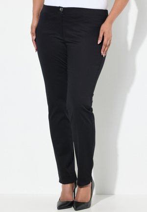Pantalones ajustados negros hechos de una tela suave, con cierre de botón en la parte delantera y diseño hasta el tobillo, combinados con tacones de punta negros.
