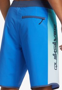 Modré plavky s gradientným dizajnom, s námorníckym pásom, so zipsovým zadným vreckom a s logom Quiksilver po boku.