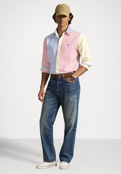 Ριγέ πουκάμισο με κουμπιά σε κόκκινο, μπλε και κίτρινο χρώμα· ανοιχτό μπλε τζιν· μπεζ καπέλο· casual ρολόι· άνετη εφαρμογή.