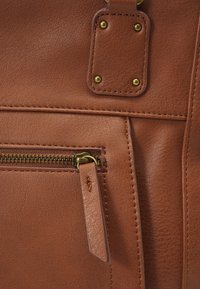 Bruine leren tas met een gestructureerd oppervlak, een gouden rits en metalen studs ter versterking. Strak ontwerp met een detail van een ritsvak.