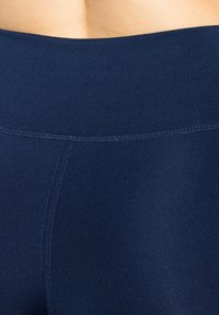 Detailní záběr na tmavě modré bezešvé legíny s vysokým pasem, které ukazují texturu a švy na látce.