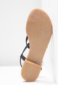 Semelle de sandale avec marquage s.Oliver en relief, semelle en caoutchouc beige avec talon texturé, brides noires visibles de côté.