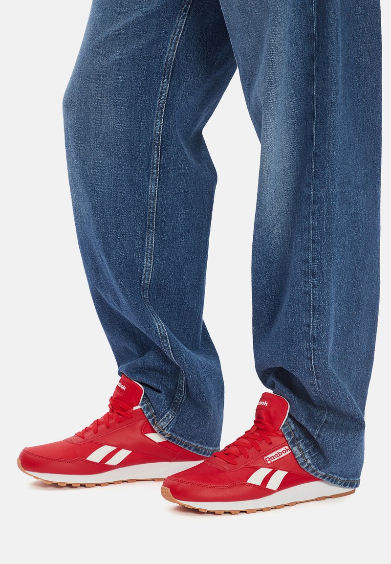 Scarpe da ginnastica rosse con dettagli e logo bianchi, con texture liscia, punta rotonda e suola imbottita, abbinate a jeans blu larghi in denim.