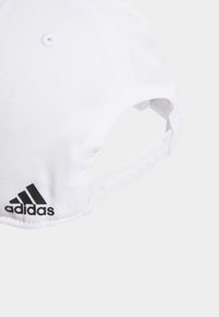 White baseball cap made of textured fabric with a curved brim. Features a black Adidas logo and an adjustable snap closure at the back.